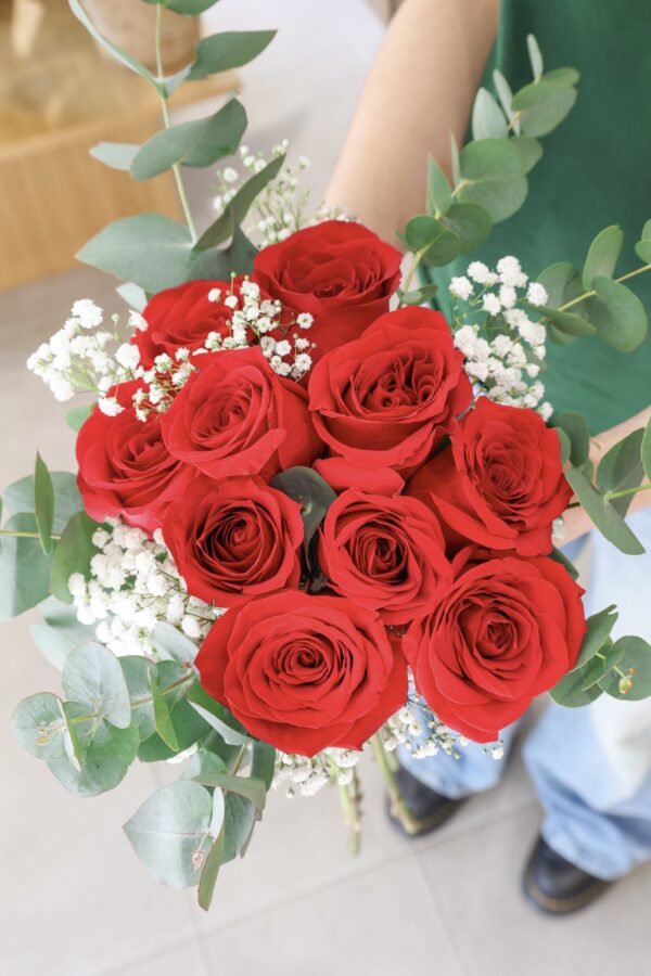 Ramo de diez rosas de color rojo sostenido por nuestra florista Júlia.