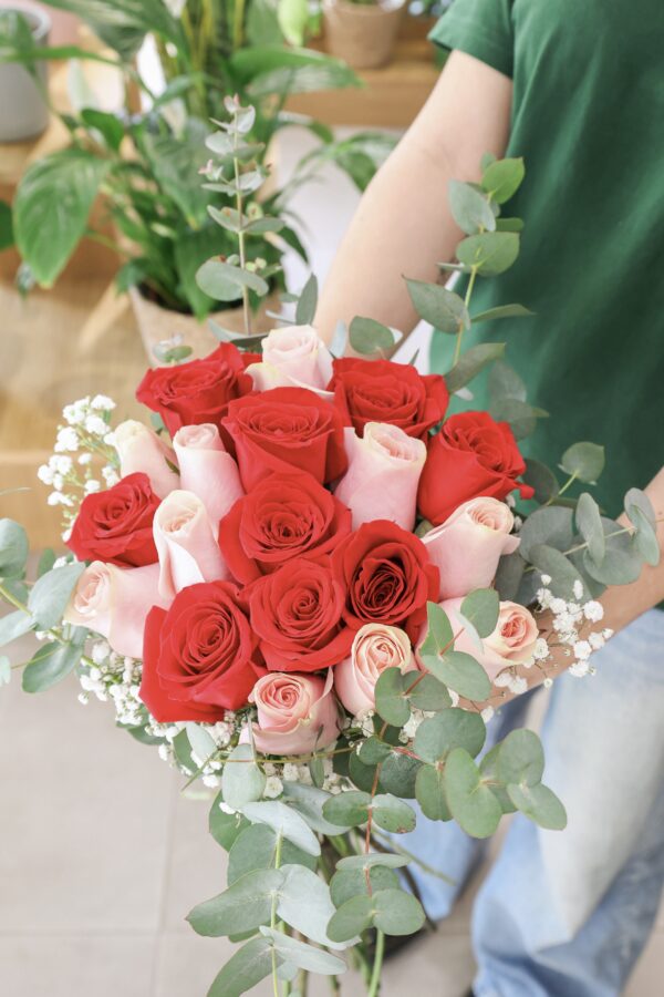 Ramo de diez rosas de color rosa y diez rosas de color rojo, sostenido por una de nuestras floristas