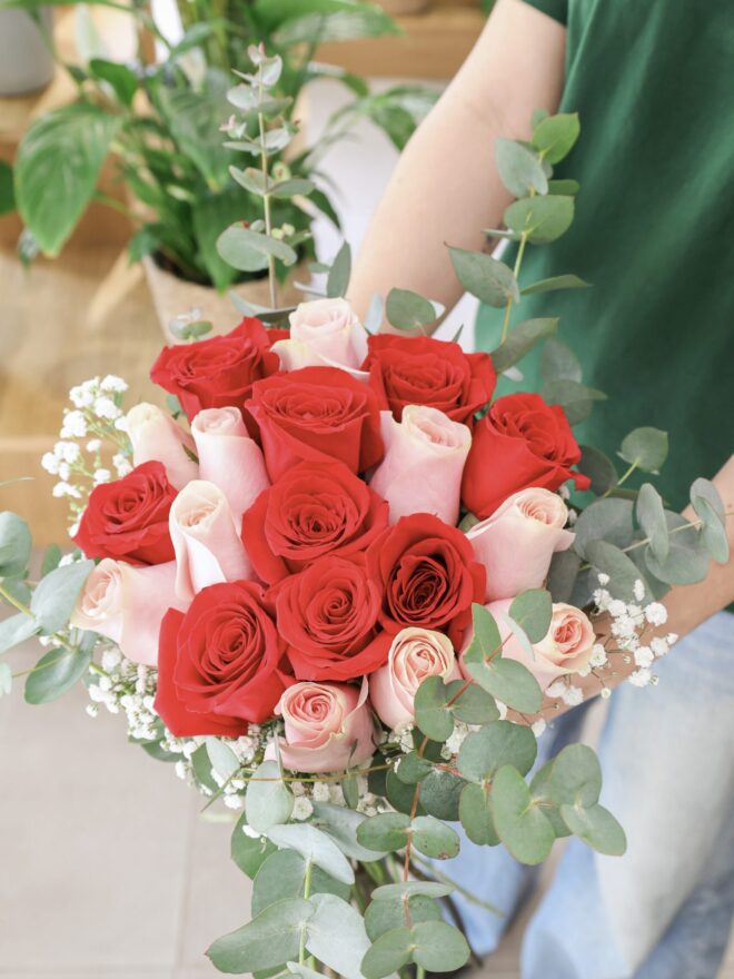 Ramo de diez rosas de color rosa y diez rosas de color rojo, sostenido por una de nuestras floristas