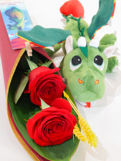 Cono de tela con 2 rosas rojas y espigas junto a peluche de dragón y punto de libro.
