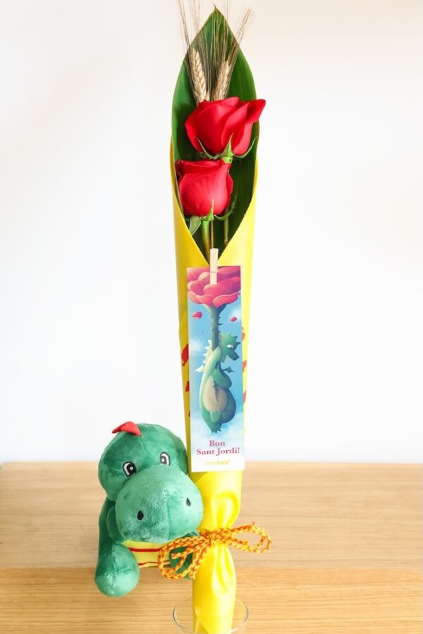 Cono de tela con 2 rosas rojas y espigas junto a peluche de dragón y punto de libro.