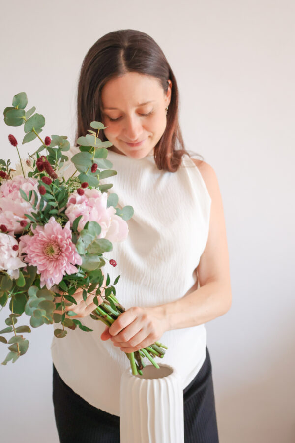 Mujer introduciendo el ramo de flores dentro del jarrón blanco