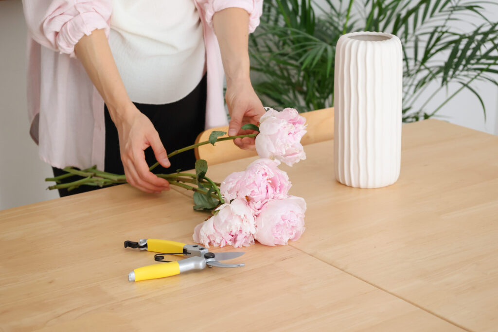 Manos preparando flores rosas junto a un jarrón