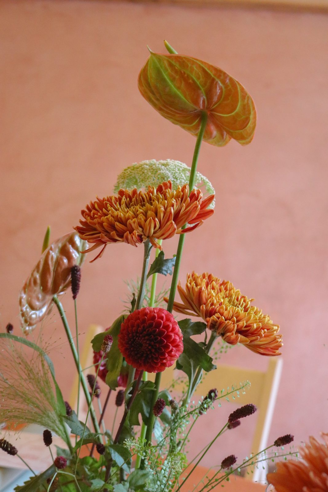 Detalle de anturios cobrizos y flores naranjas y granates sobre el fondo terracota de Casa Vicens